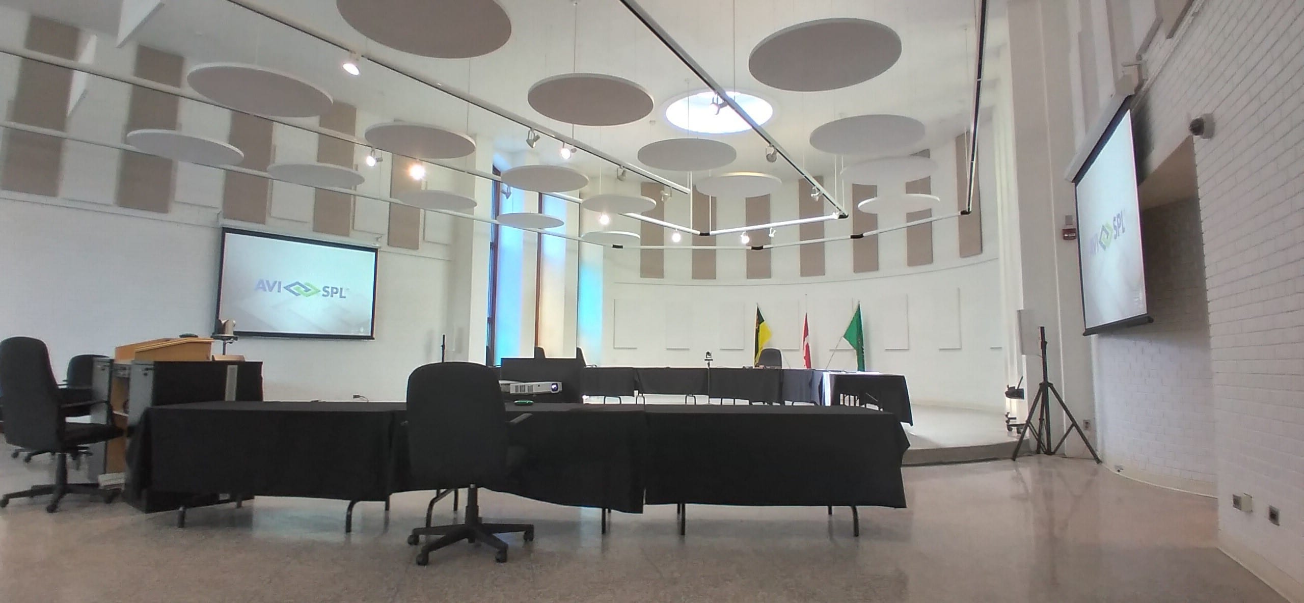 Modern conference room with circular ceiling, sound panels, large screen, flags by a long table—ready for a meeting.