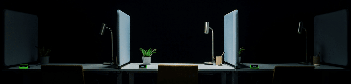 Dim office: two desks with lamps, plants, and gadgets; dark backdrop highlighting lit areas.
